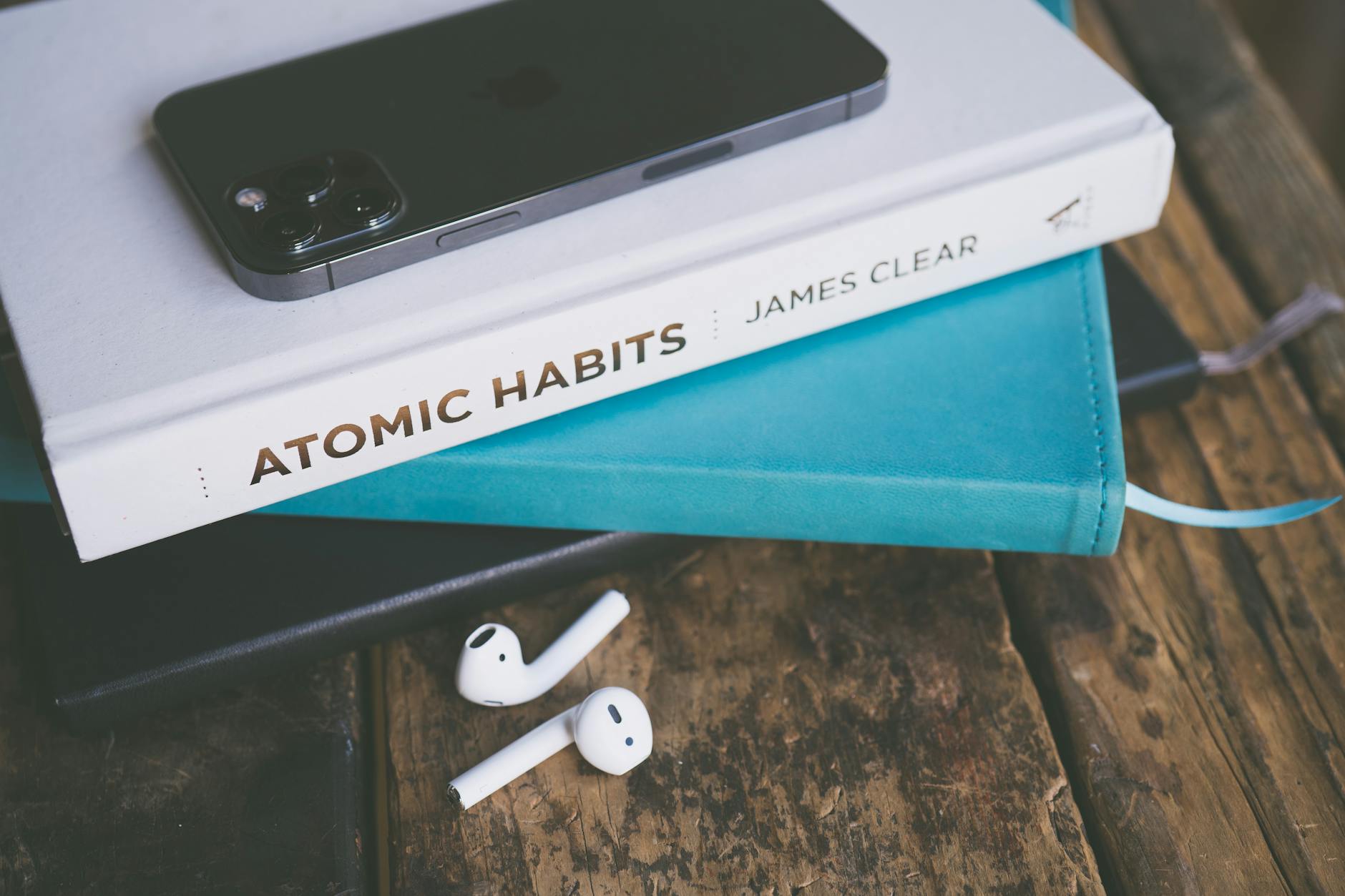 An elegant arrangement of a smartphone, book, and AirPods on a wooden table. (Photo by Jessica Lewis 🦋 thepaintedsquare on Pexels)