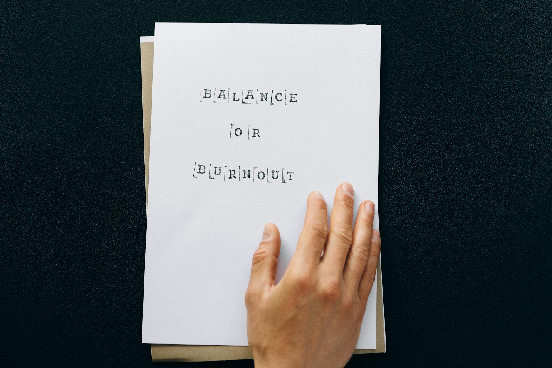 Hand holding paper with 'Balance or Burnout' text, promoting mental wellness. (Photo by Nataliya Vaitkevich on Pexels)