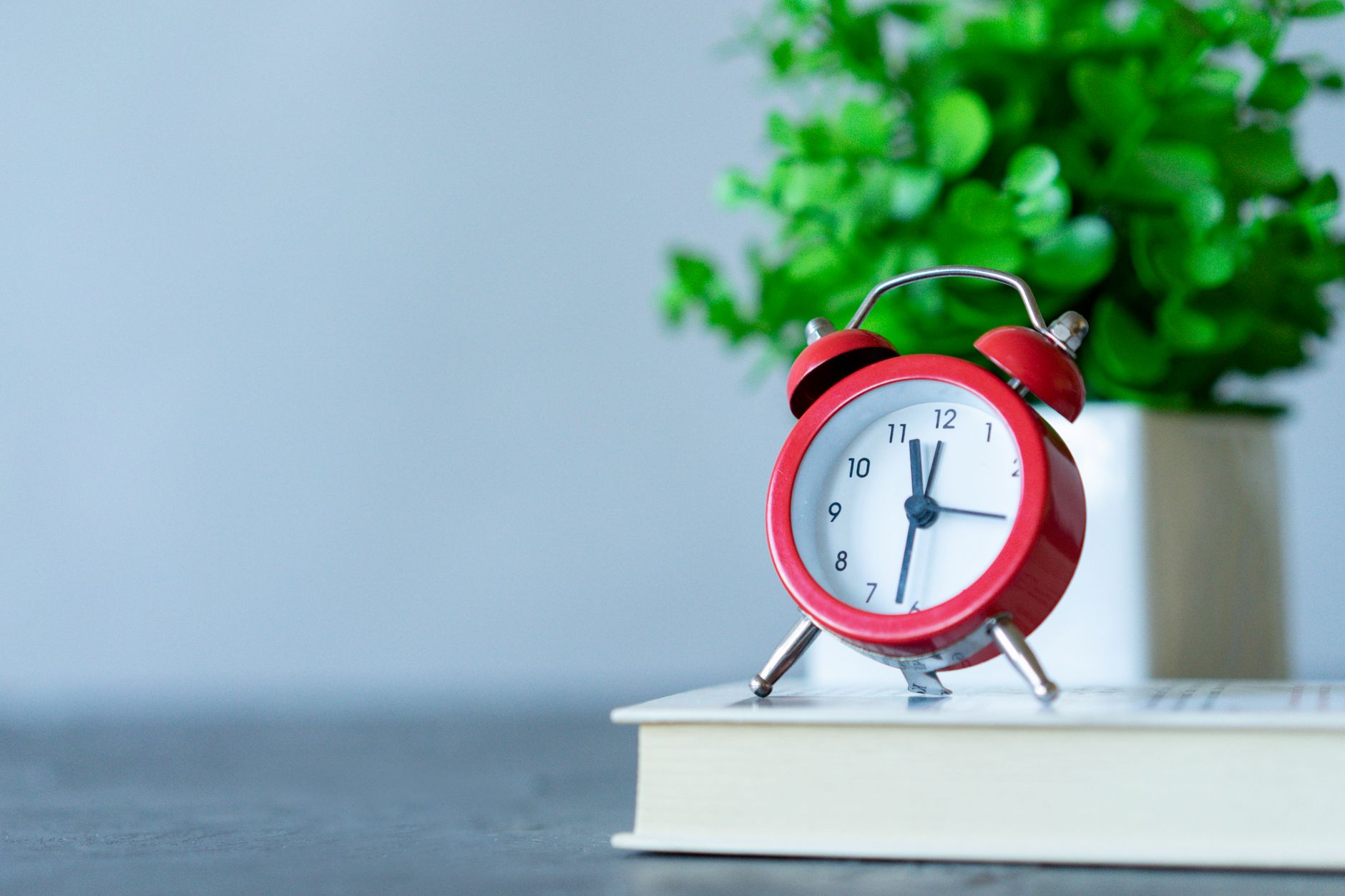 Image of a red alarm clock on a book with a green plant in the background. (Photo by Atlantic Ambience on Pexels)