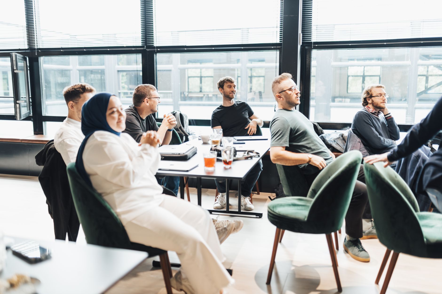 Modern office setting with diverse team in discussion, seated around a table by large windows. (Photo by Matheus Bertelli on Pexels)