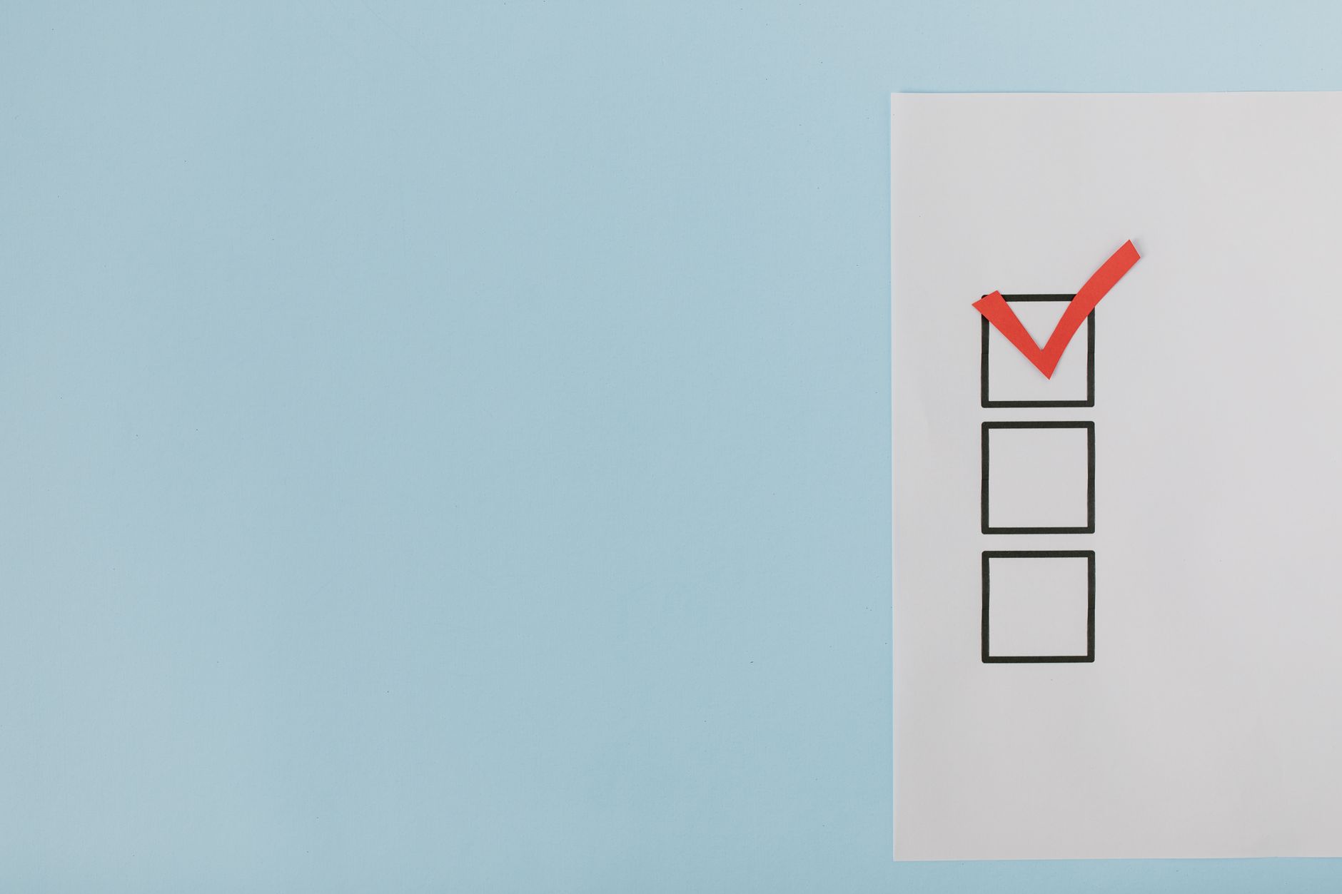 A minimalist checklist with a red checkmark on a blue background, providing ample copy space. (Photo by Tara Winstead on Pexels)